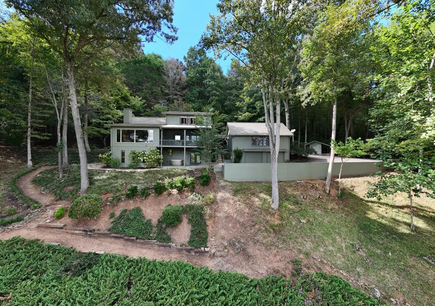 Main house exterior seen from across the sloped driveway, surrounded by wooded hillside