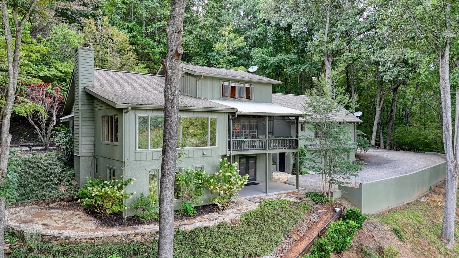 Main house facade with a two-story wall of windows, framed by trees along the winding driveway