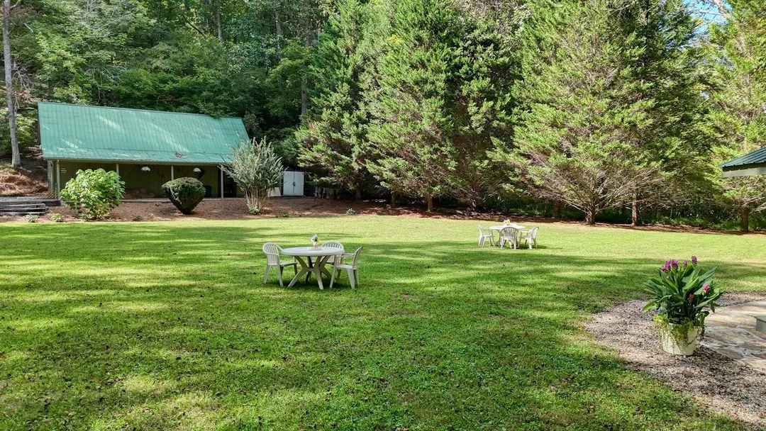 Broad mowed lawn with round tables and chairs, the barn and tall trees behind