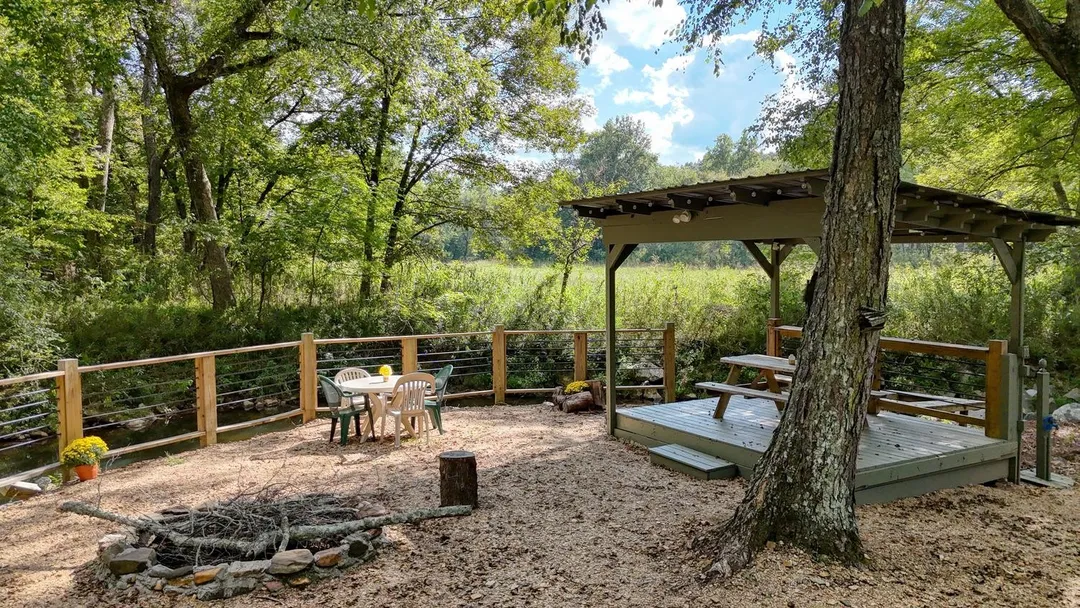 Stone fire ring beside a covered creekside deck with a picnic table
