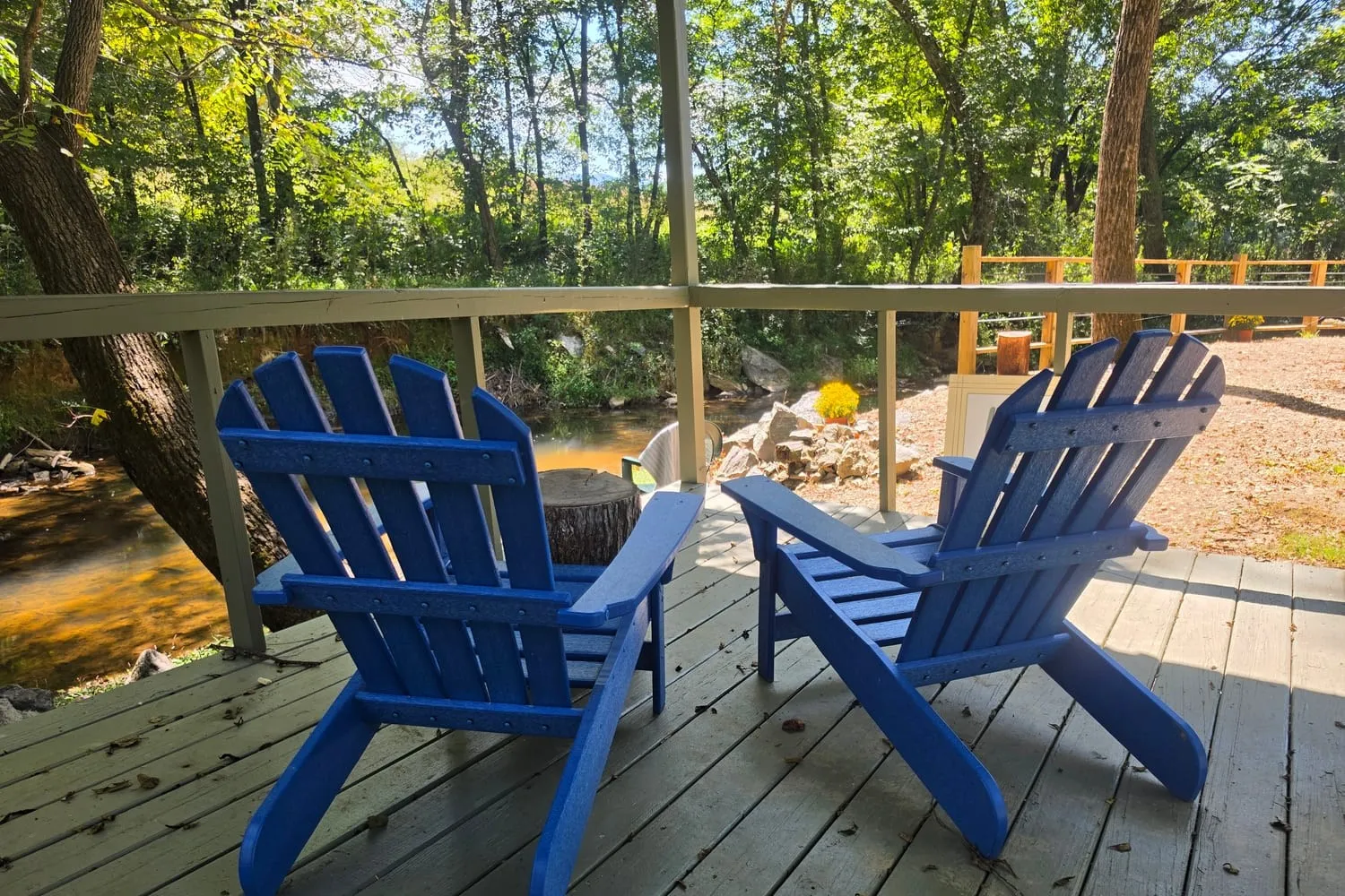 Blue Adirondack chairs on a covered deck above the creek