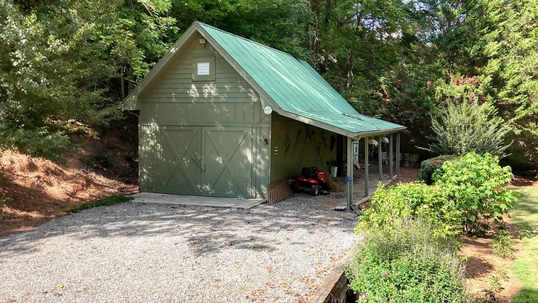 Green barn with a metal roof, double doors and an open lean-to beside a gravel area
